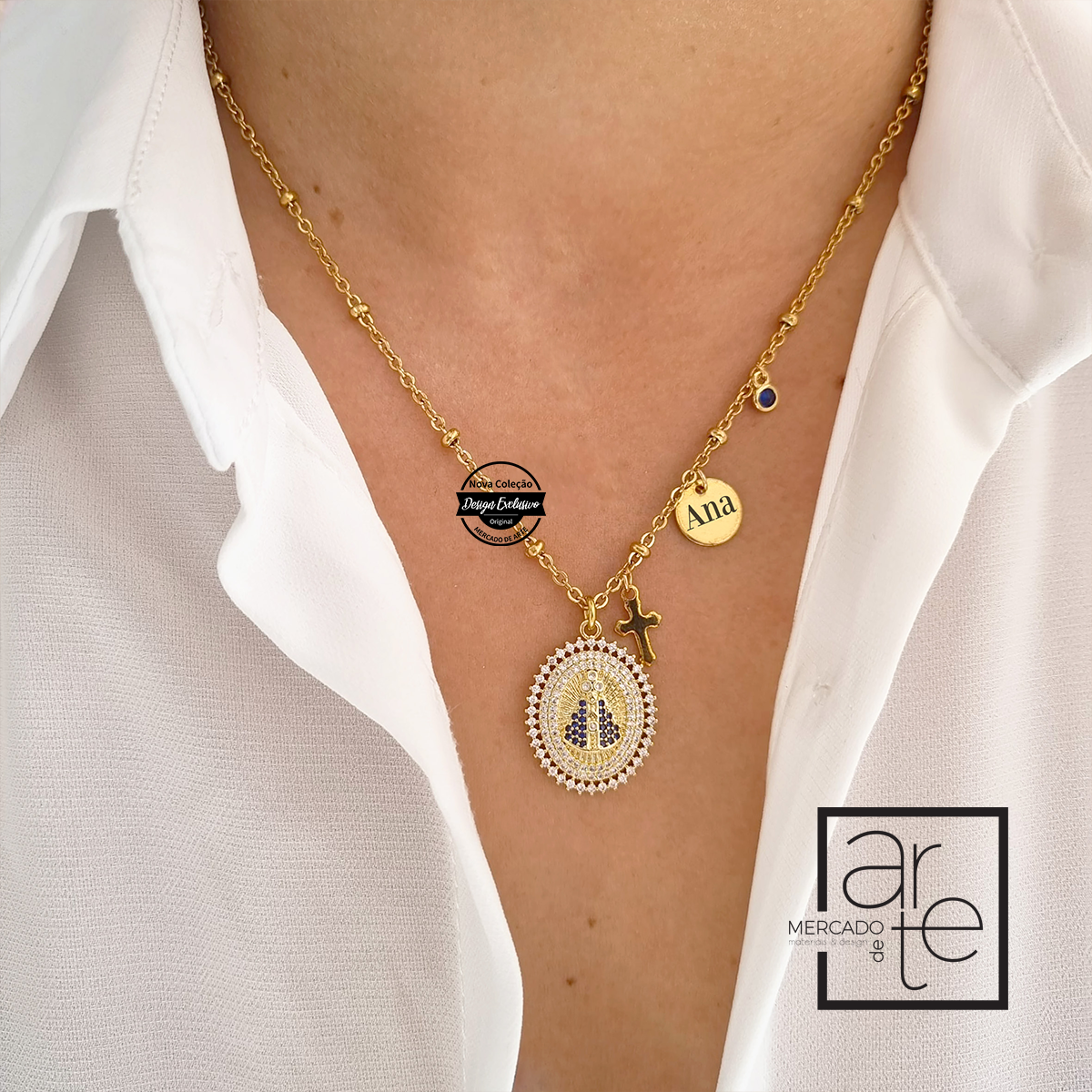 Fio em aço inoxidável dourado com medalhão de santa ornamentado por mini zircónias brancas e azuis com pendente cruz e brilhante azul. Pode personalizar a medalhinha com nome ou iniciais.